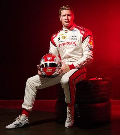 Josef Newgarden sitting on a tire stack and holding his racing helmet