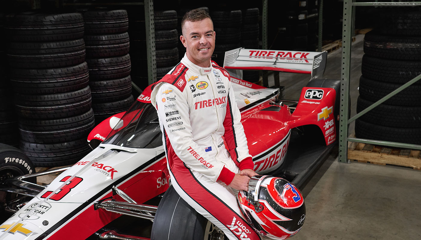 Scott McLaughlin sitting on the Penske-branded number 3 car in the Tire Rack warehouse