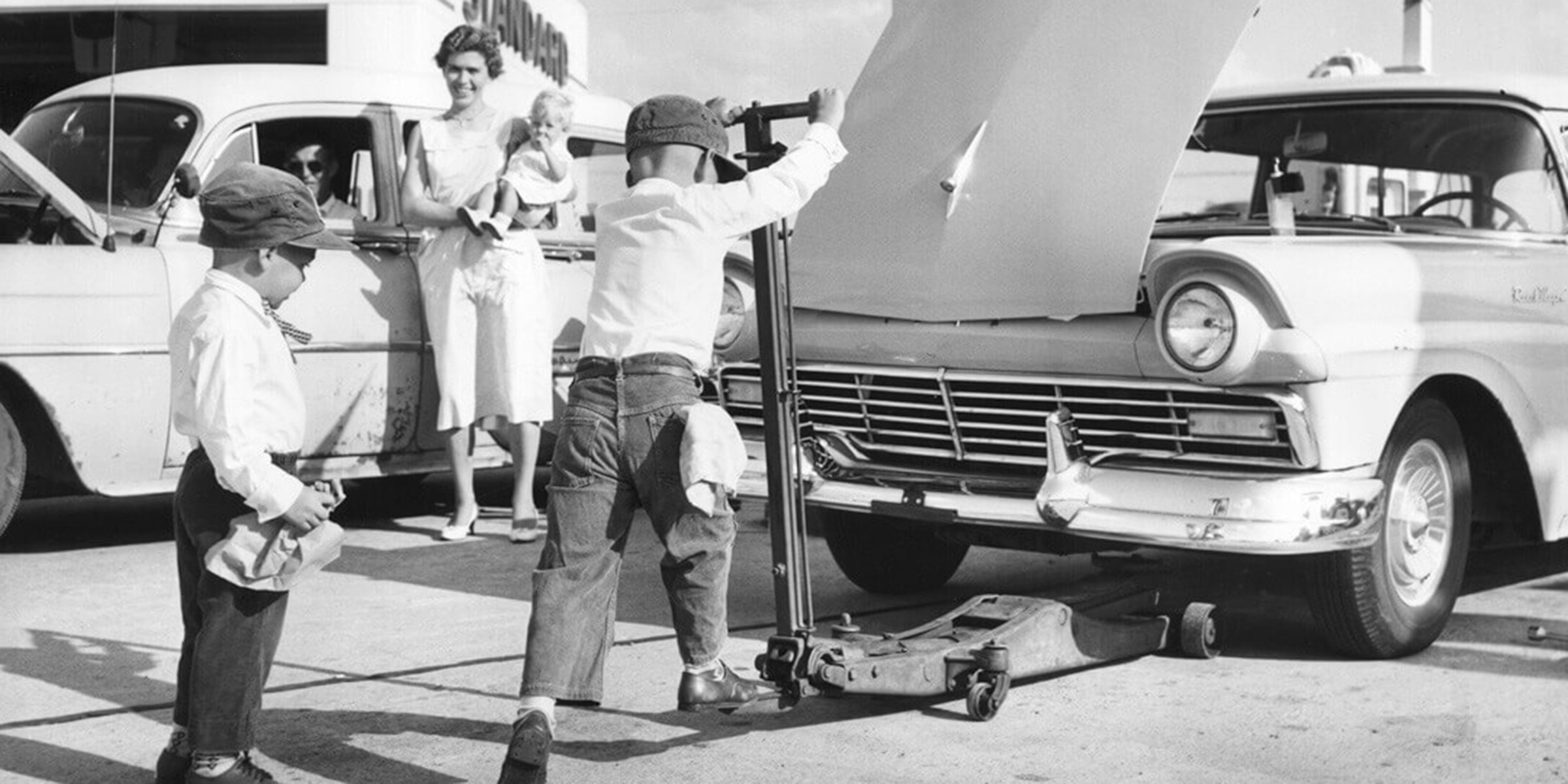 Vintage photo of two boys working under a classic car at a service station, capturing the spirit behind Over 40 Years of Tires.