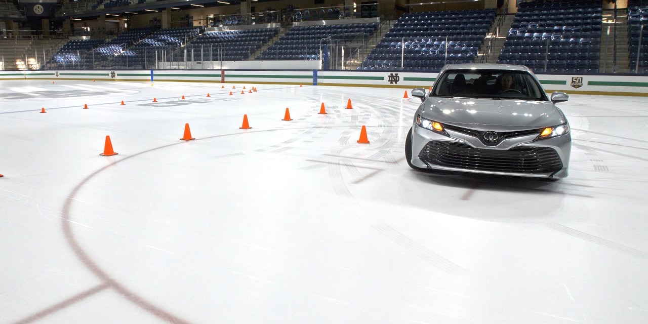A silver Toyota Camry driving on an ice rink through a course of orange cones.