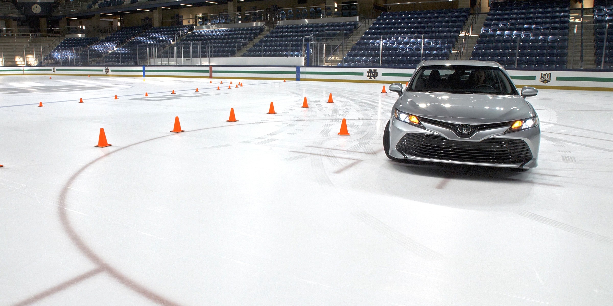 A silver Toyota Camry driving on an ice rink through a course of orange cones.