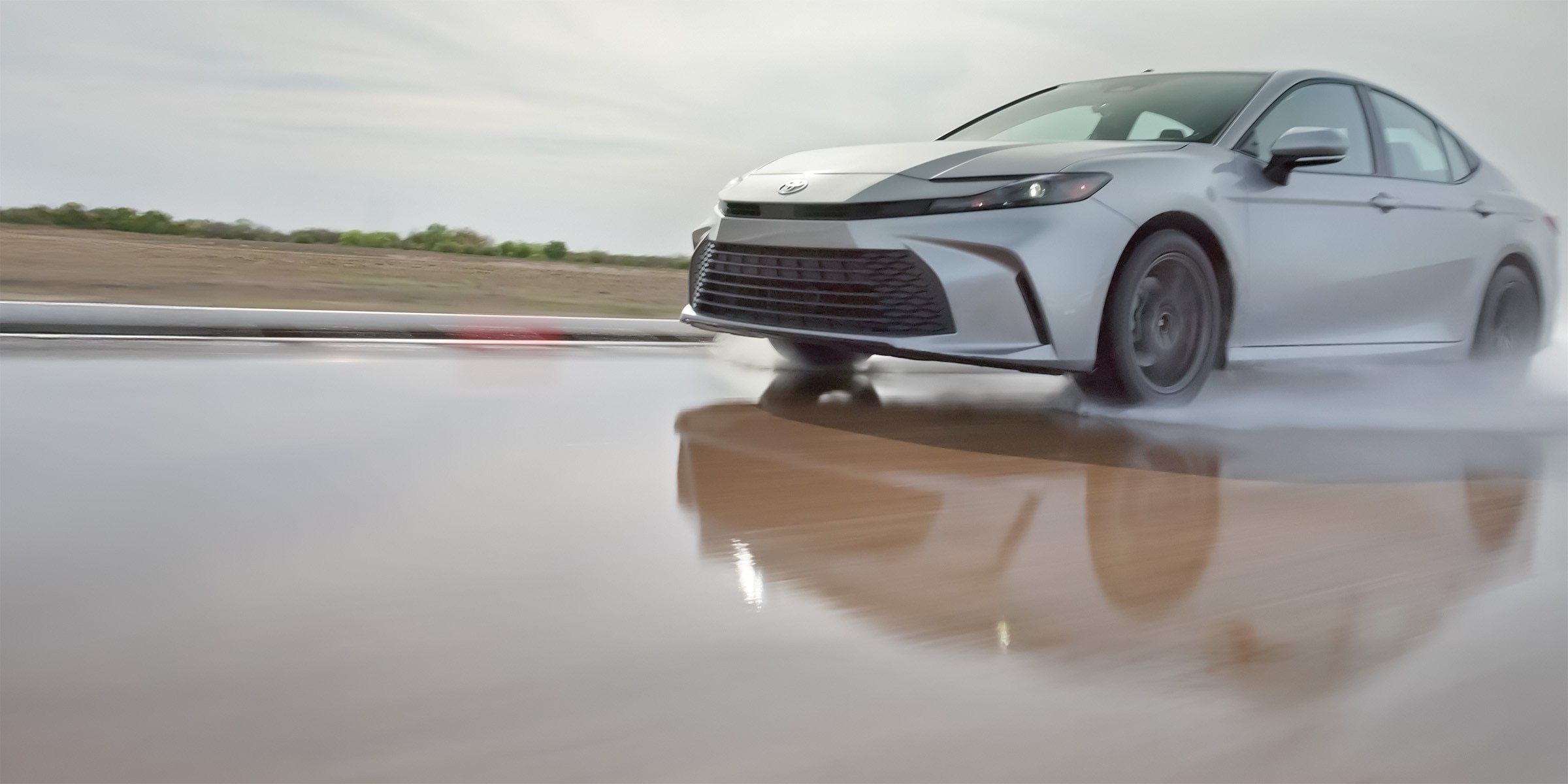 A silver Toyota Camry driving on a wet track with water spraying from the tires.