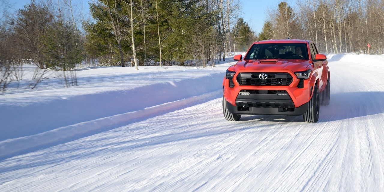 A red Toyota Tacoma driving on a snowy road during winter testing.