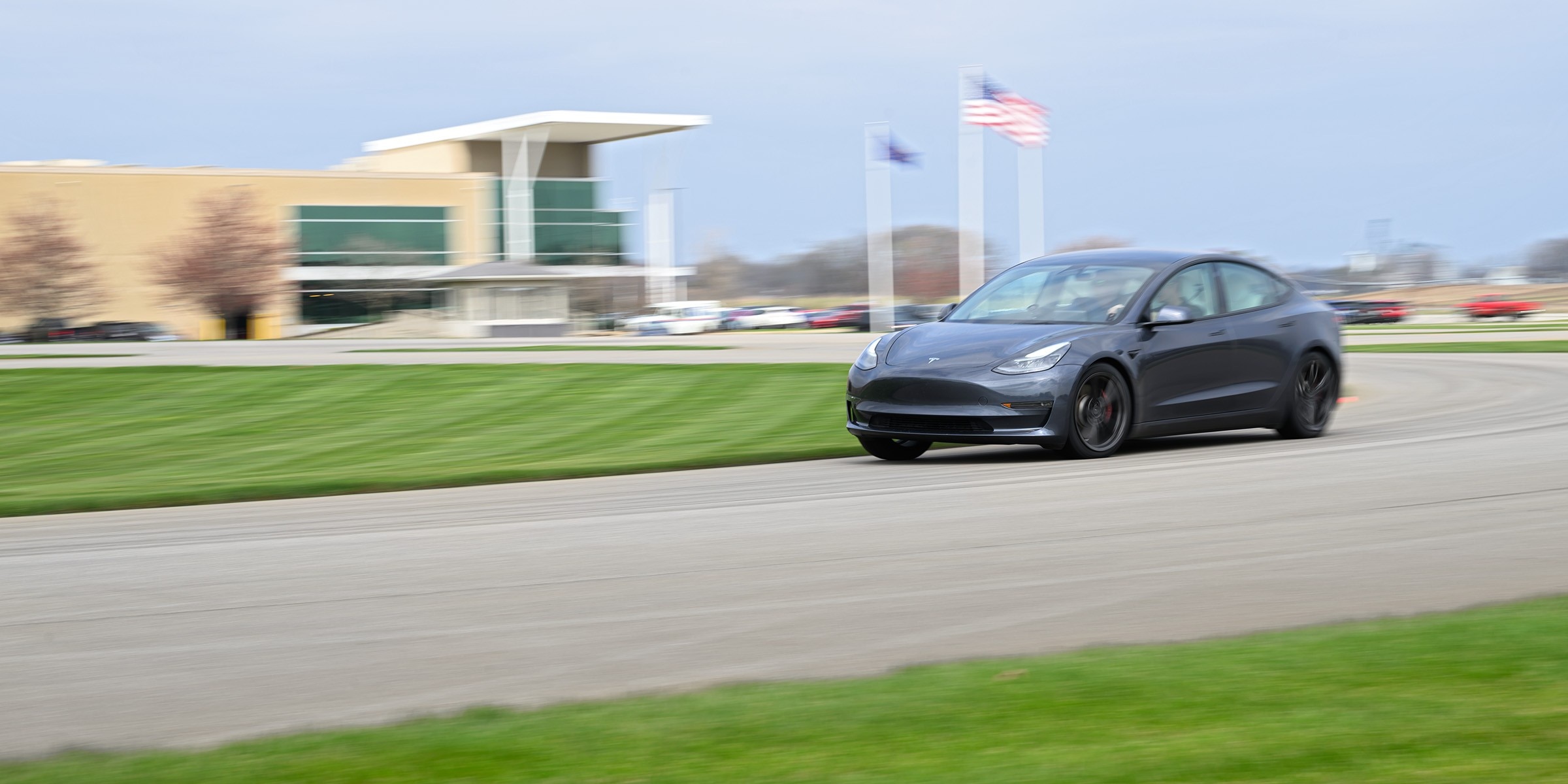 A gray Tesla Model 3 driving quickly around a paved test track.