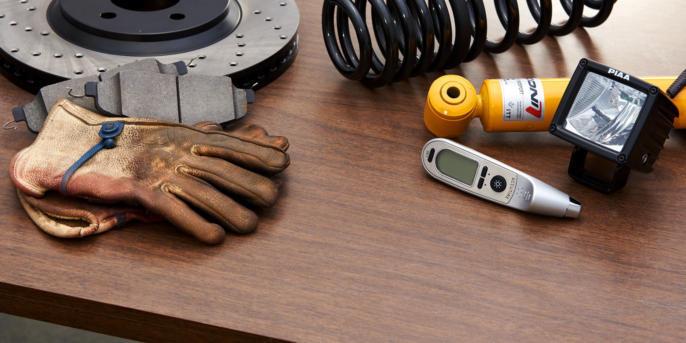 StopTech rotor and brake pads, Koni shock, springs, PIAA light, gloves, and tire gauge on wood table