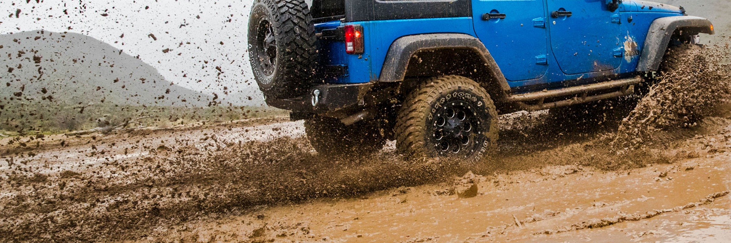 Blue Jeep splashing through mud with Firestone Destination M/T2 tires.
