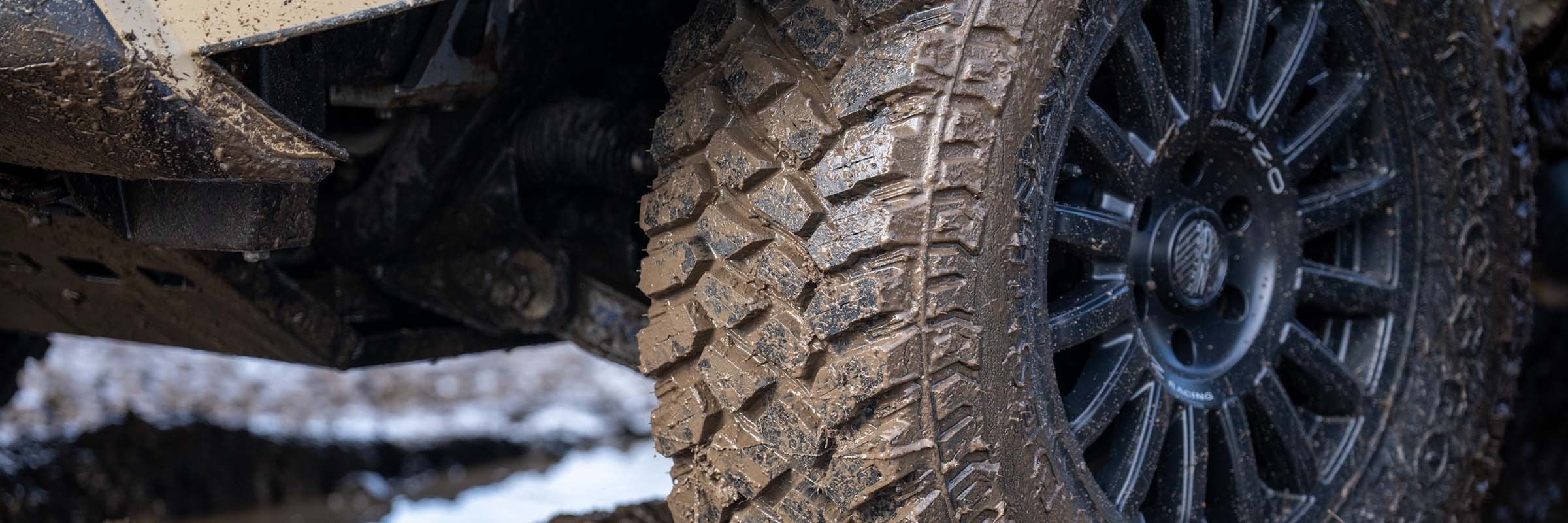 Close-up of a mud-terrain tire tread on a dark wheel covered in dirt.