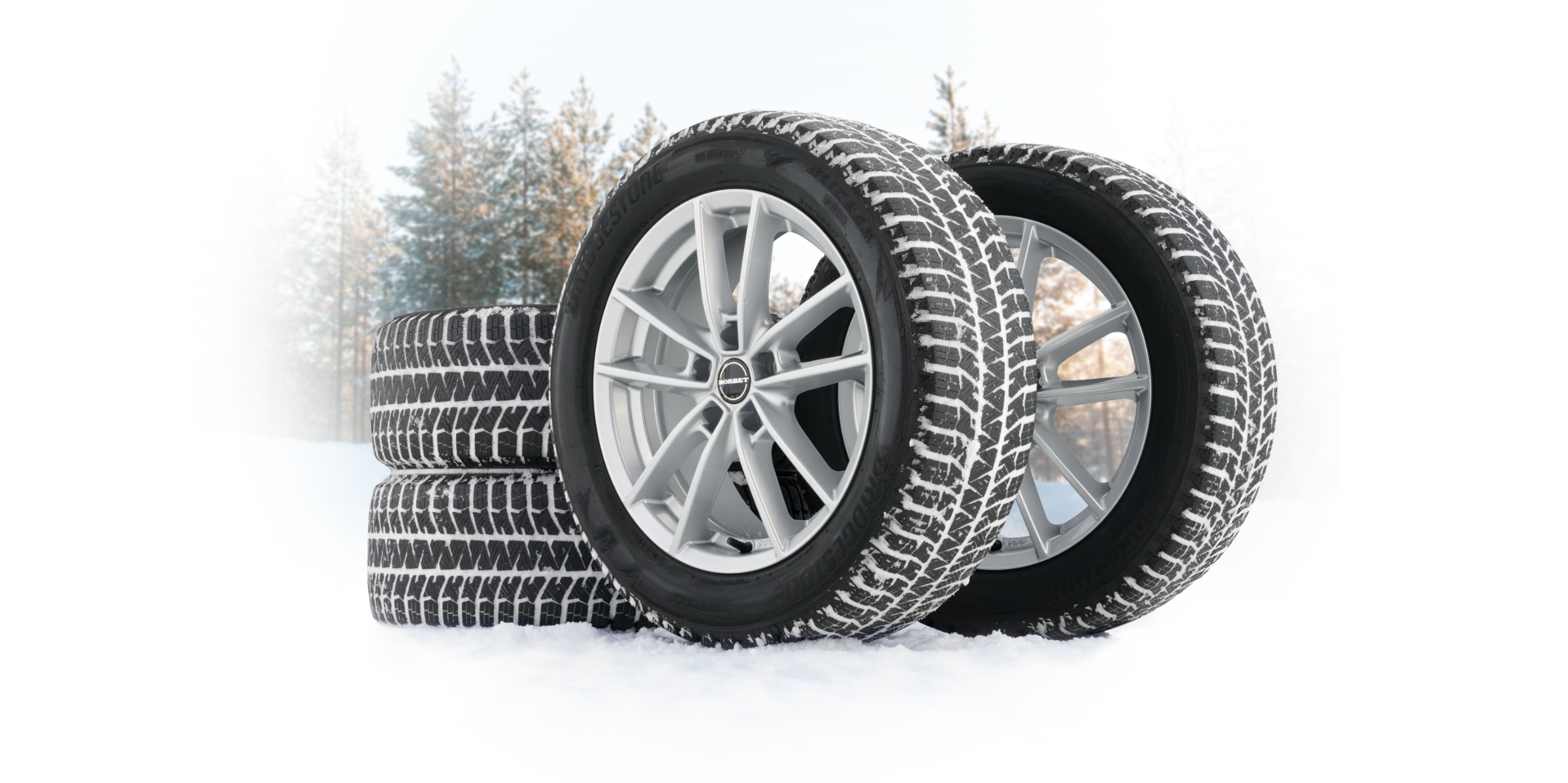 Stack of winter / snow tire & wheel package displayed on snowy ground