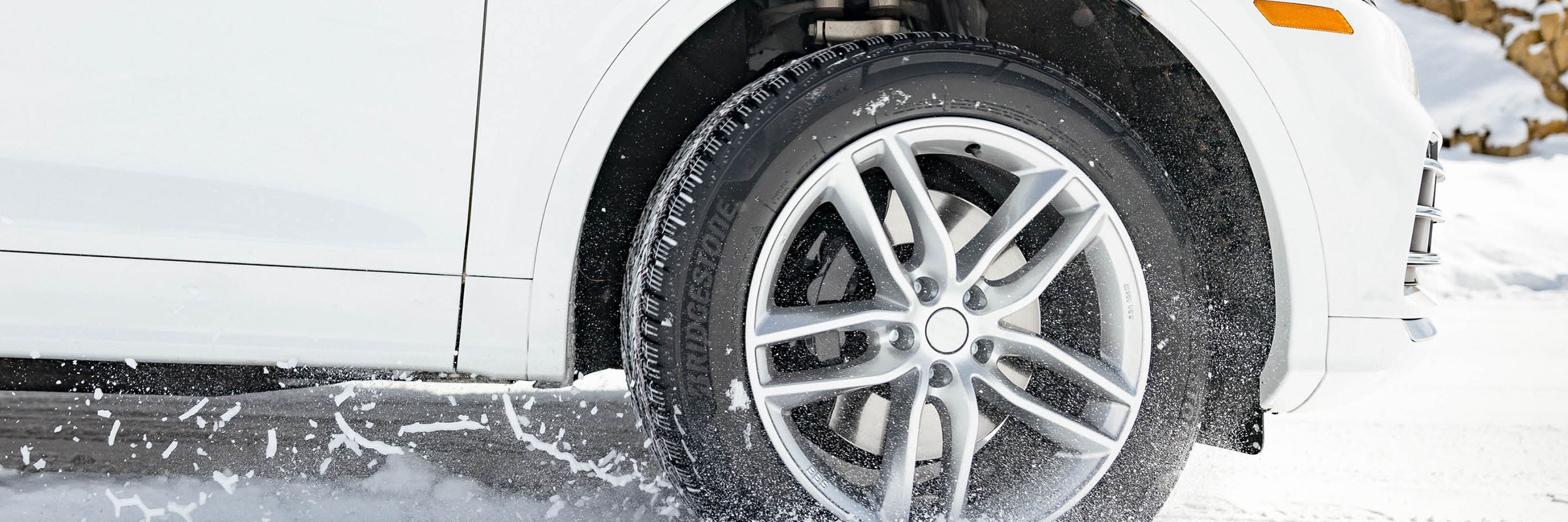 Bridgestone WeatherPeak all-weather tire driving through snow on a white vehicle.