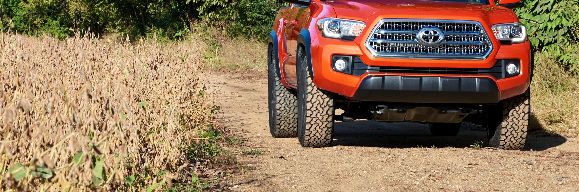 Orange Toyota Tacoma driving on a dirt road with General Grabber A/TX tires.