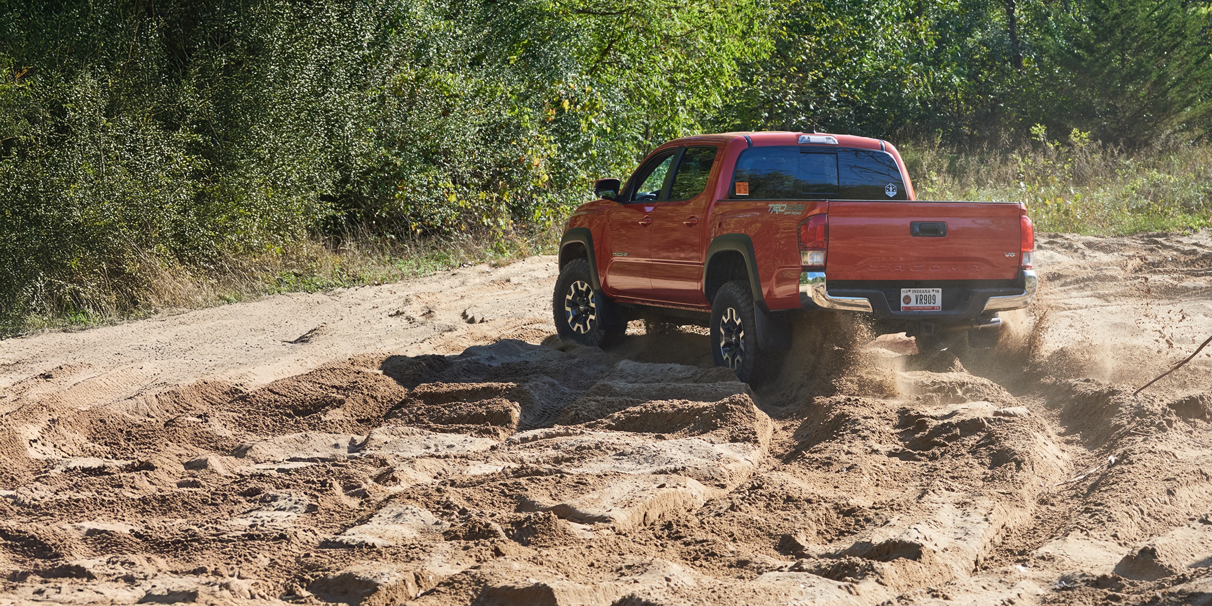 Red pickup truck driving through deep sand demonstrating off-road and all-terrain tire traction.
